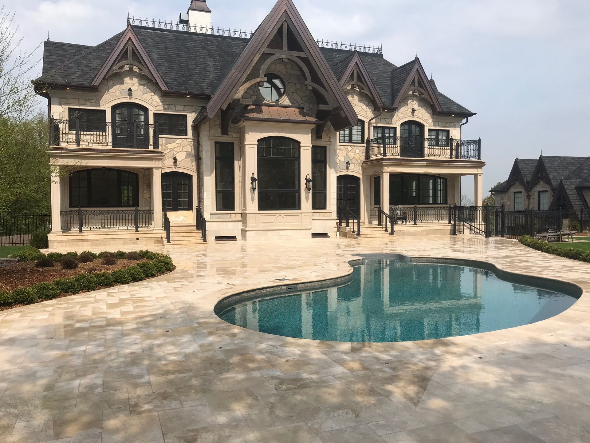 A large stone mansion with a pool, balconies, and ornate roof against a cloudy sky.