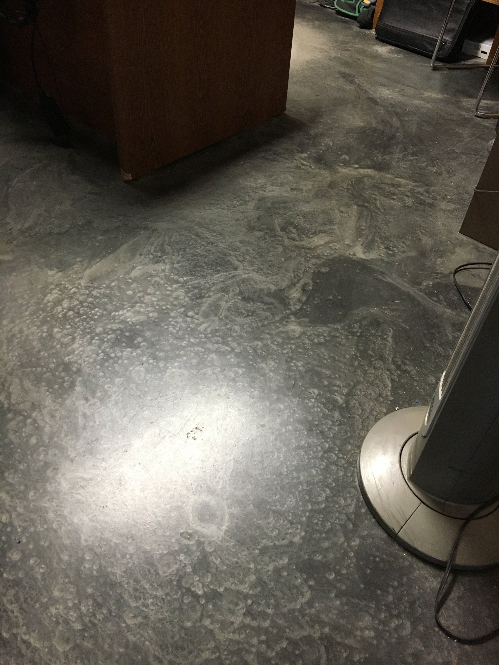 A dirty concrete floor with a fan on it in a room.