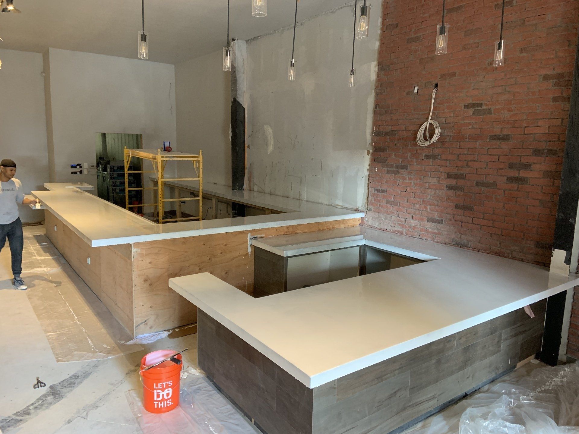 A man is standing in a room with a long counter and a bucket.