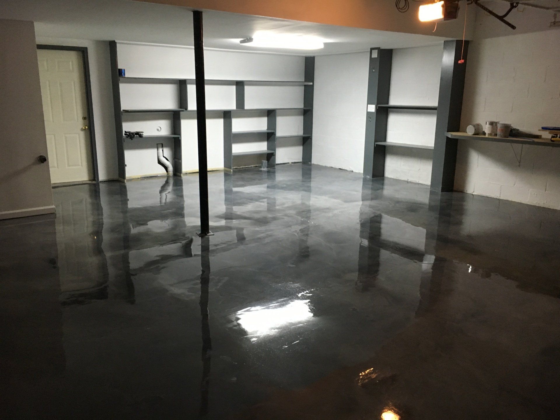A basement with a shiny metallic floor and shelves.