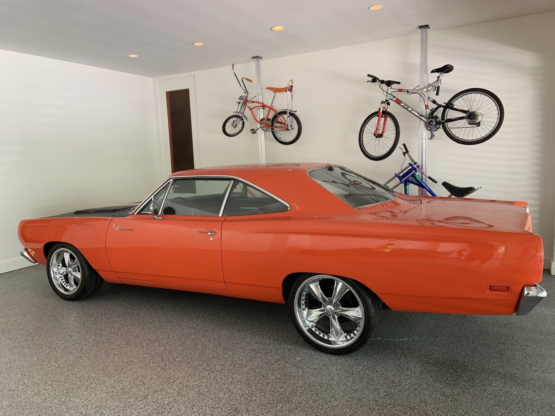An orange car is parked in a garage next to two bicycles