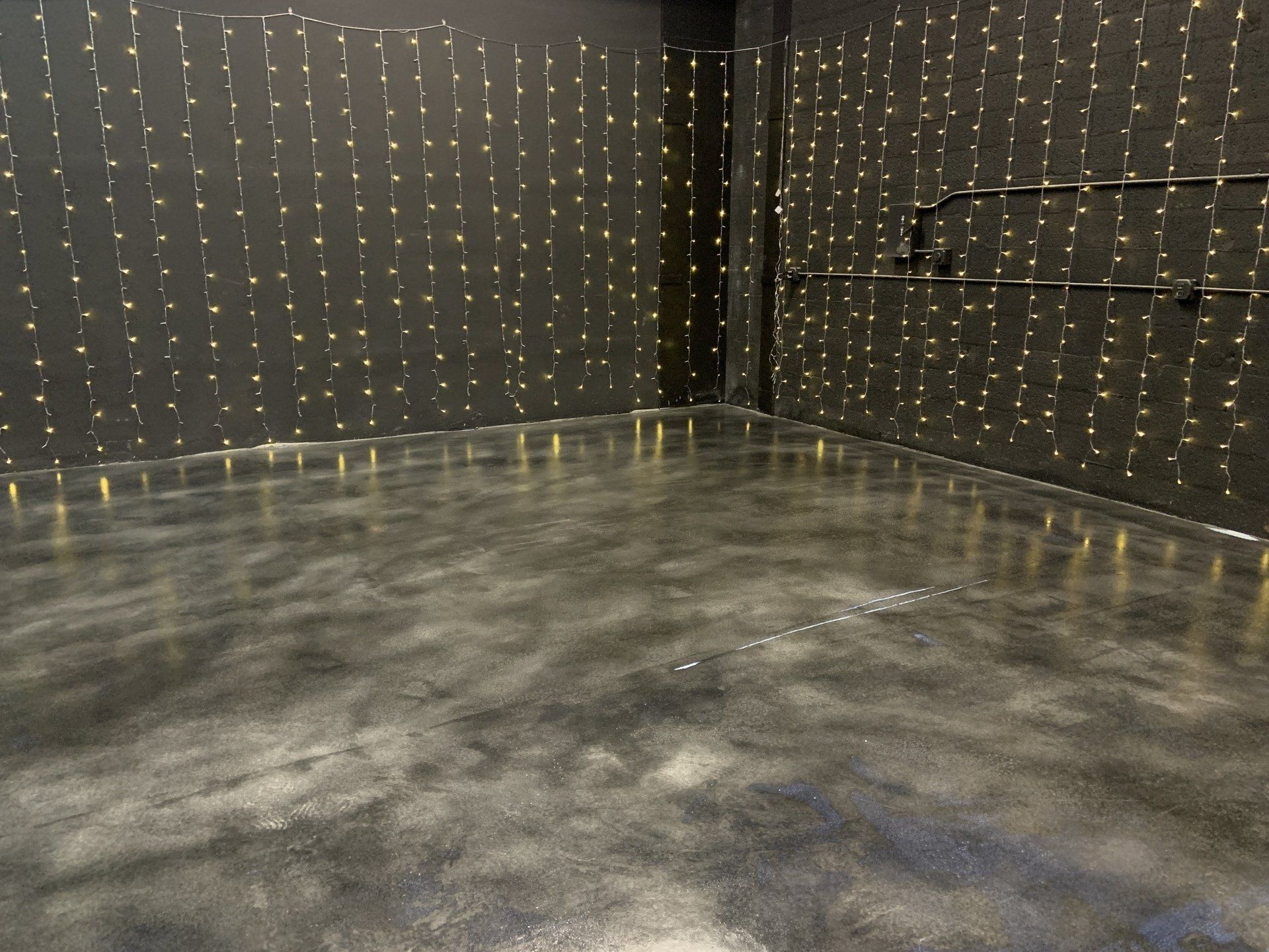 A room with a concrete floor and a black wall with lights on it.