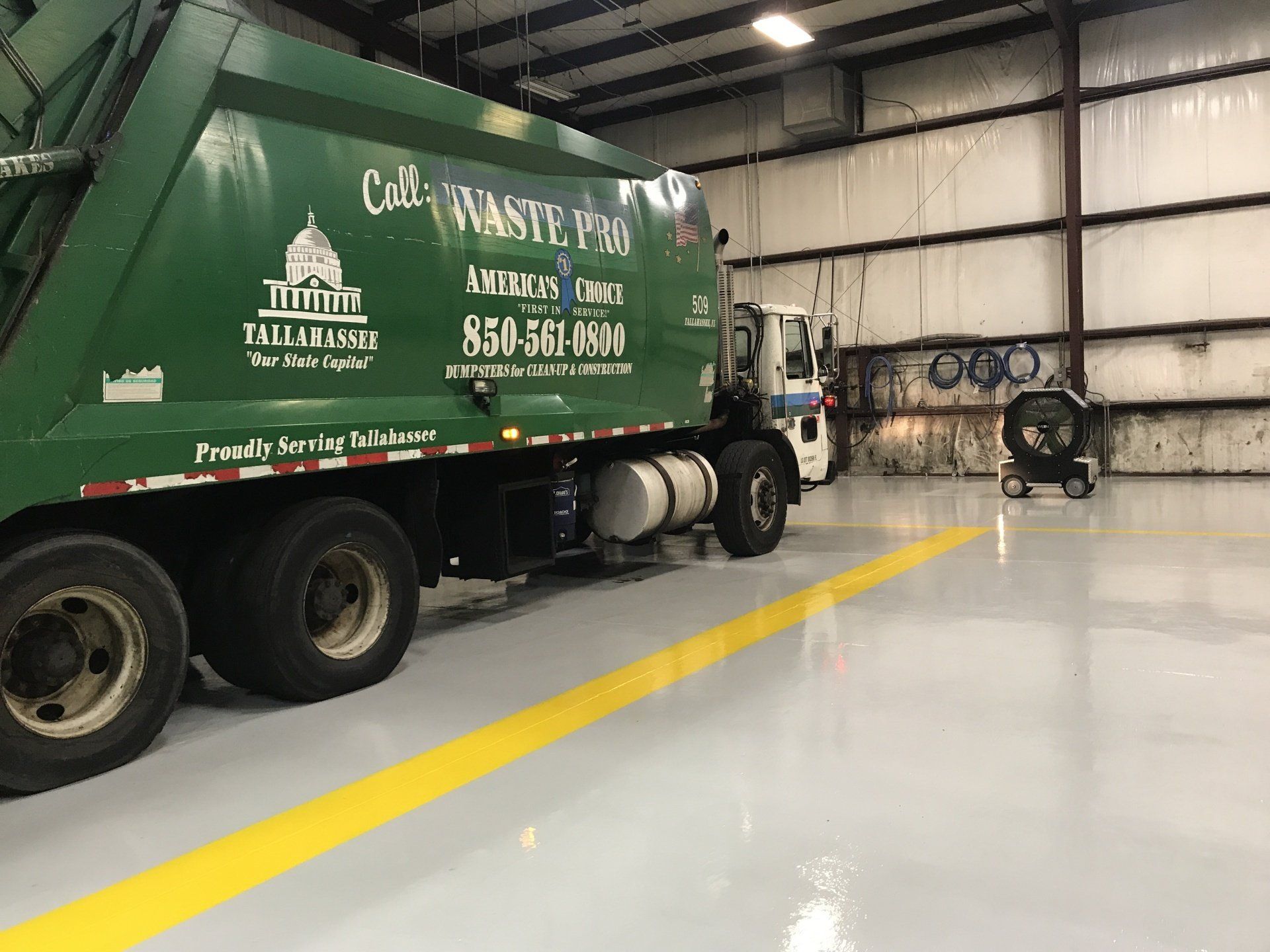 A green garbage truck is parked in a garage.