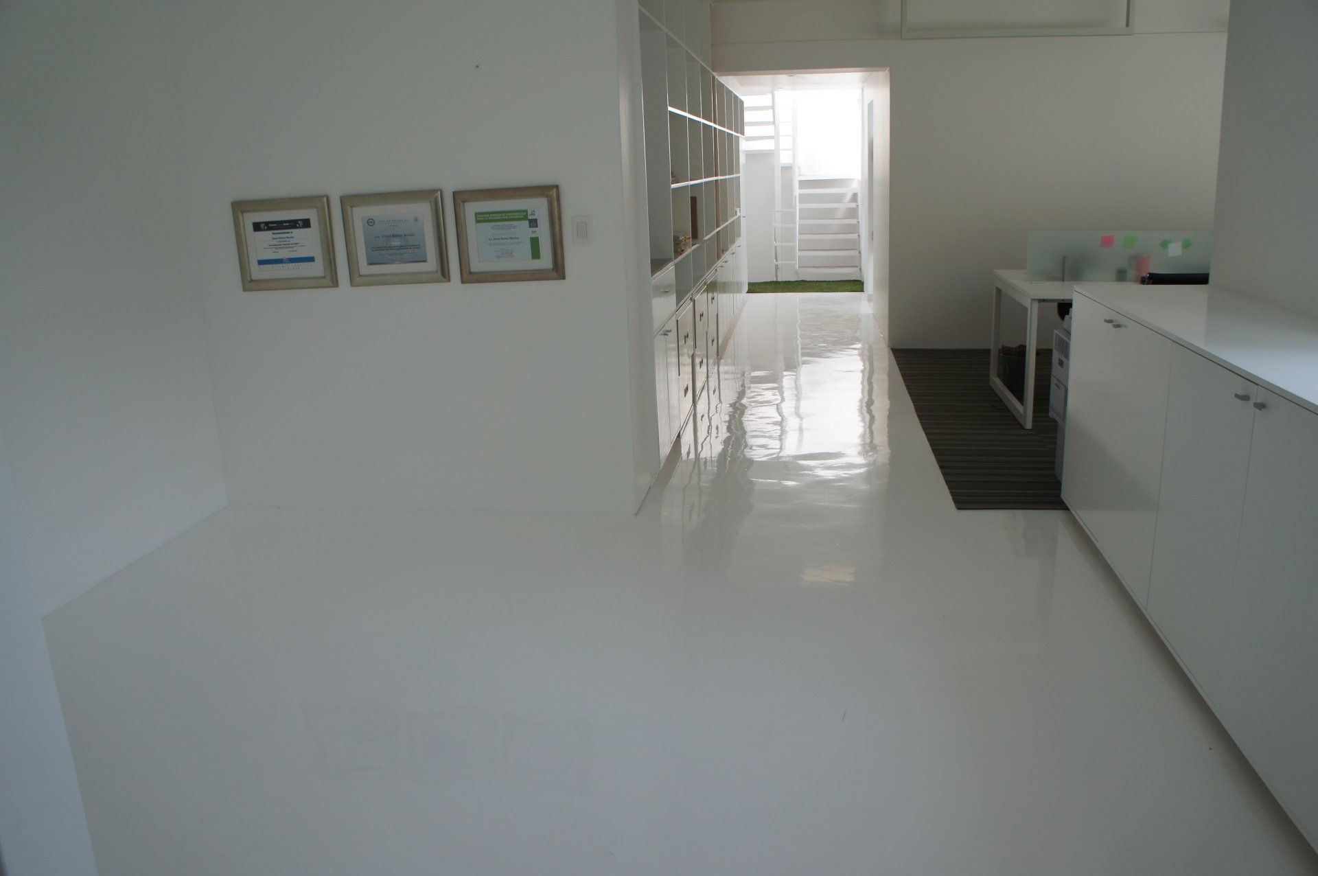 A hallway with a white floor and a few pictures on the wall