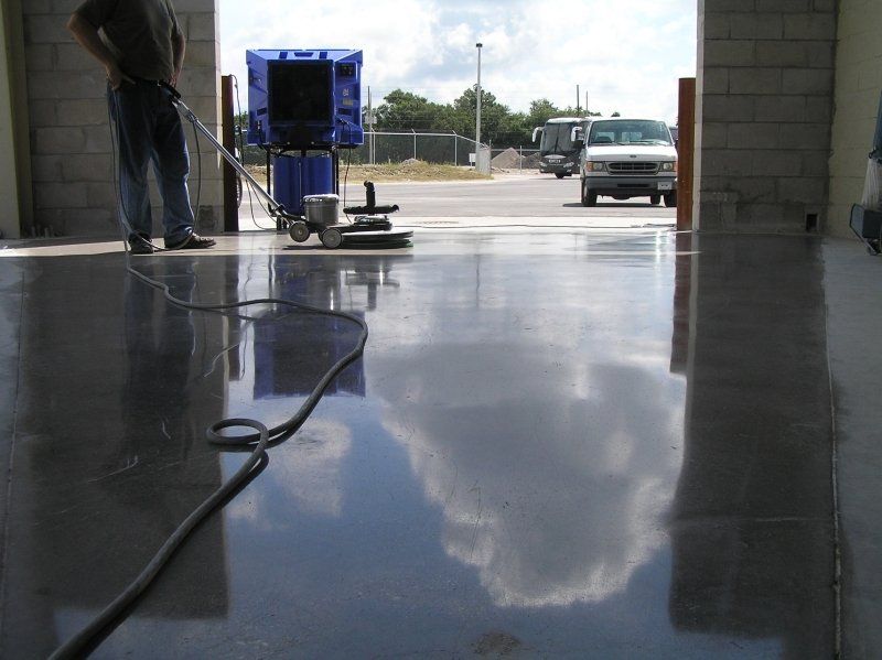 A man is cleaning a shiny concrete floor with a vacuum cleaner