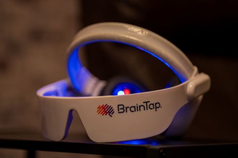 BrainTap headset: white device with blue lights, resting on a surface, logo visible. brain training. meditation. stress relief