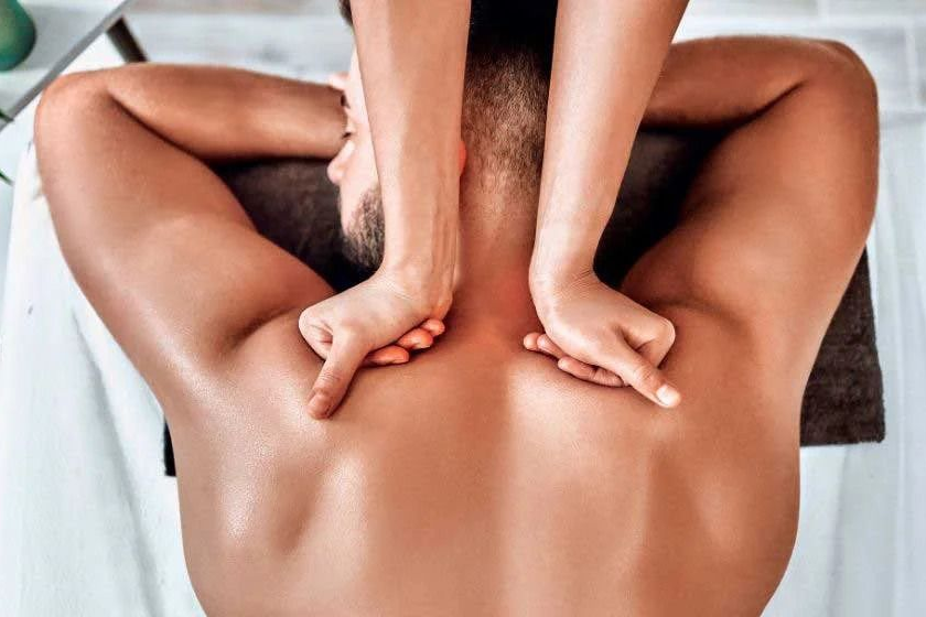 Hands massaging a man's back and shoulders; he is face down on a massage table. deep tissue massage