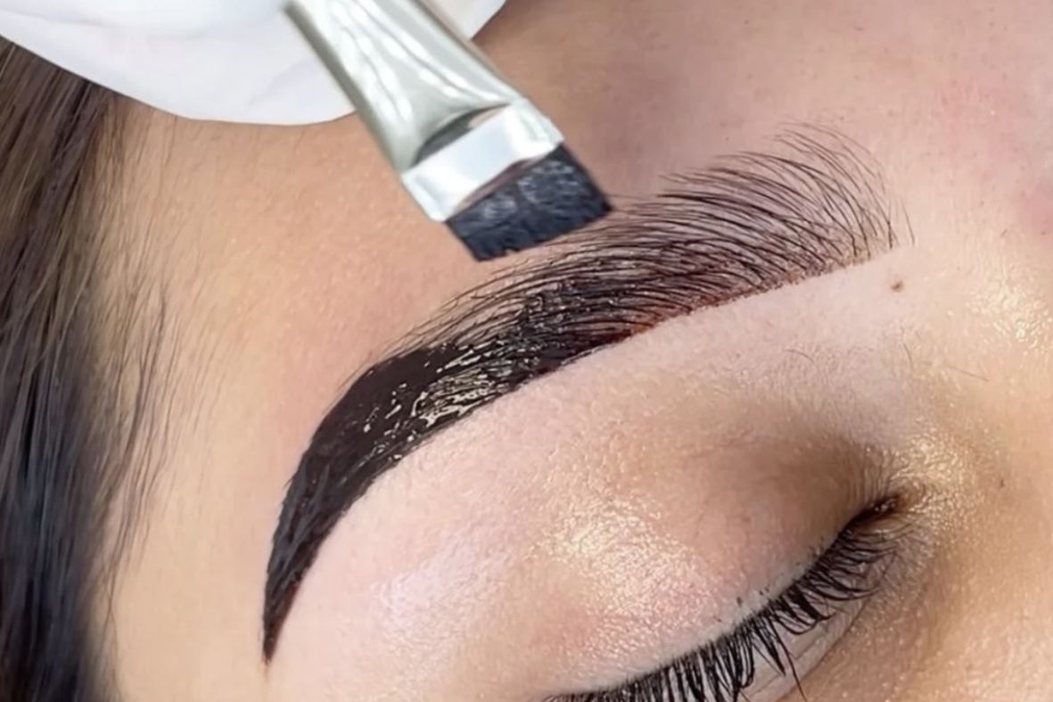 A person getting their eyebrow tinted. A brush applies dark dye to the eyebrow. eyebrow tint