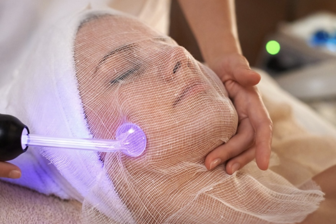 Woman receiving facial treatment with a handheld high-frequency device, covered with a gauze.