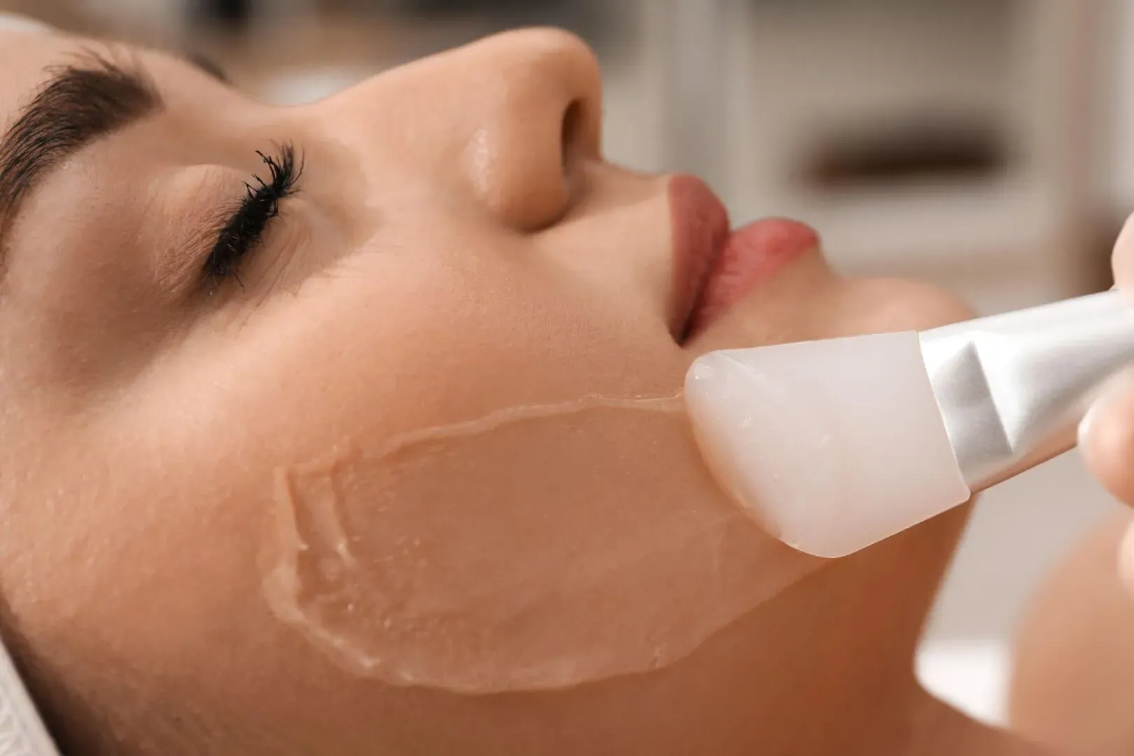 A woman with closed eyes has a facial mask applied to her face with a brush. skin polish facial