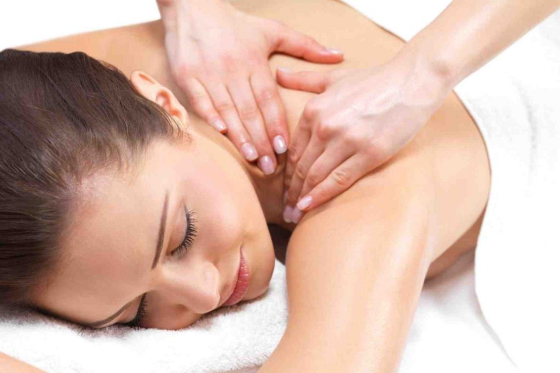 Woman receiving a shoulder massage; hands kneading her back; white towel, spa setting. swedish massage