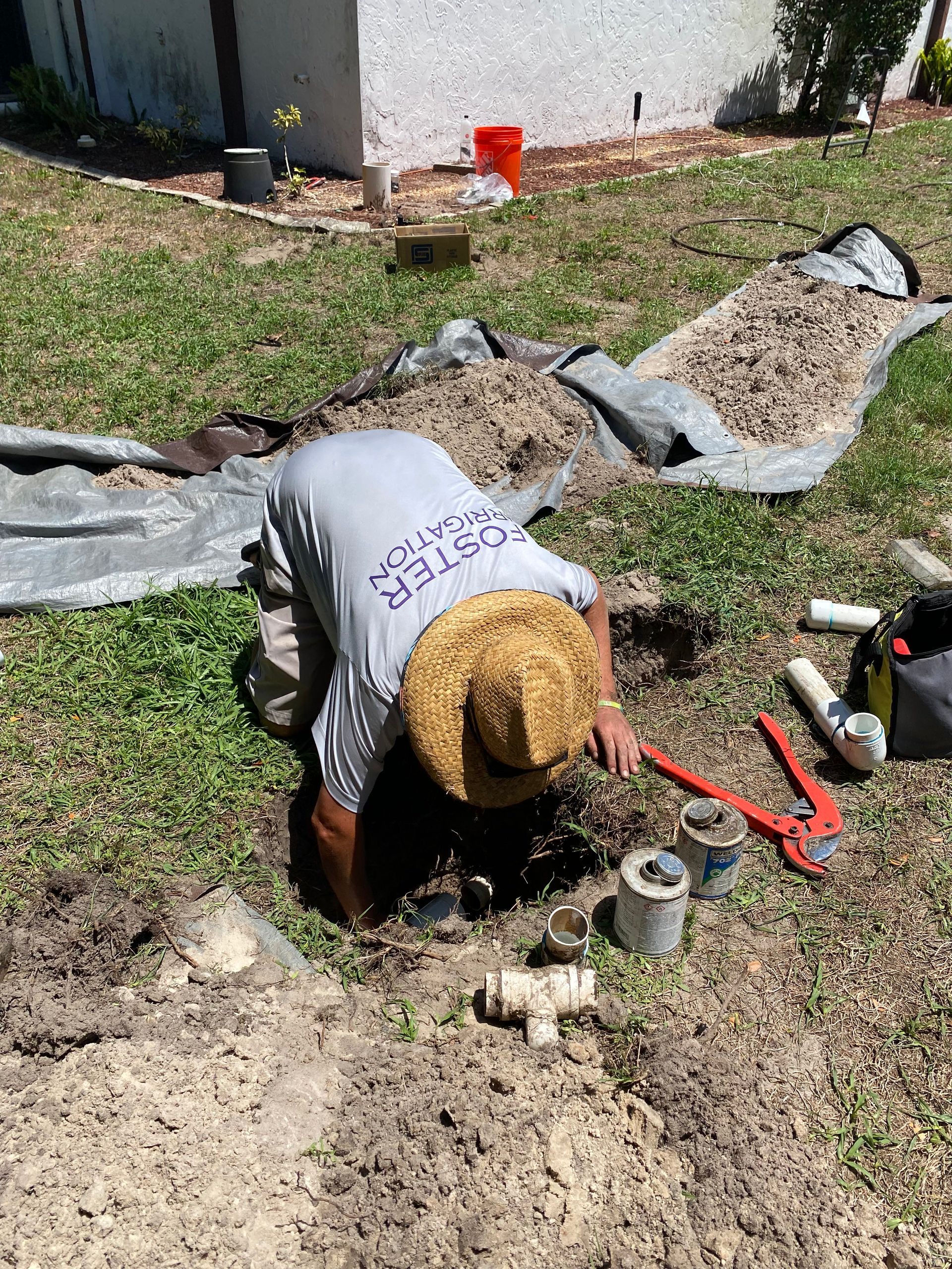 A man wearing a straw hat is kneeling down in the dirt.