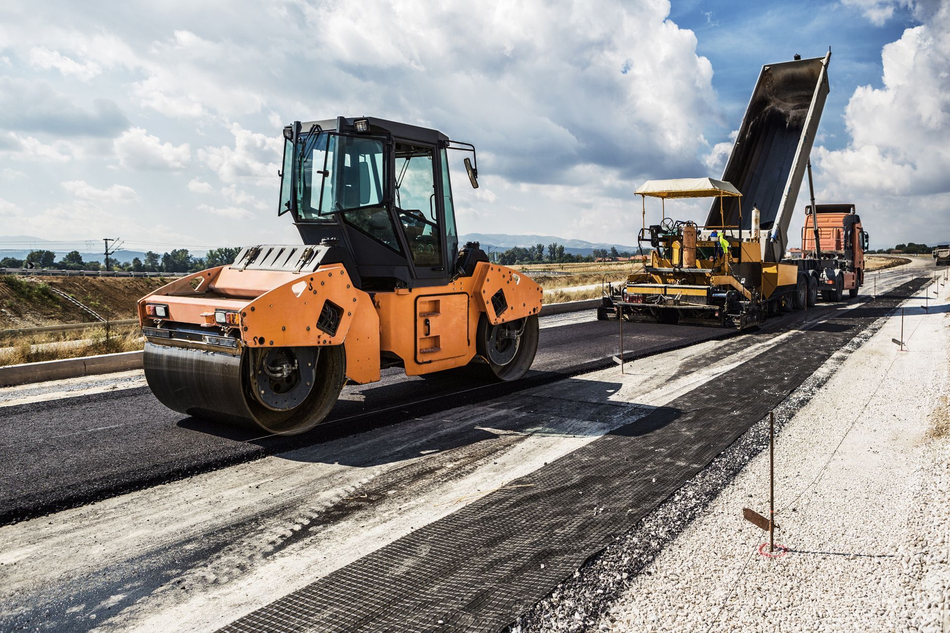 A road is being paved with a roller and a dump truck