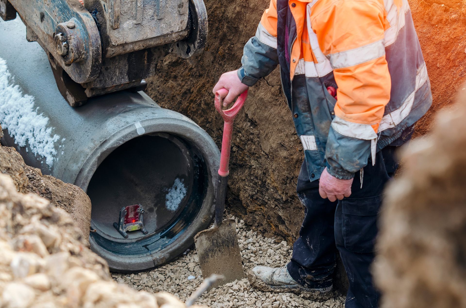 A man is digging a hole in the ground next to a pipe