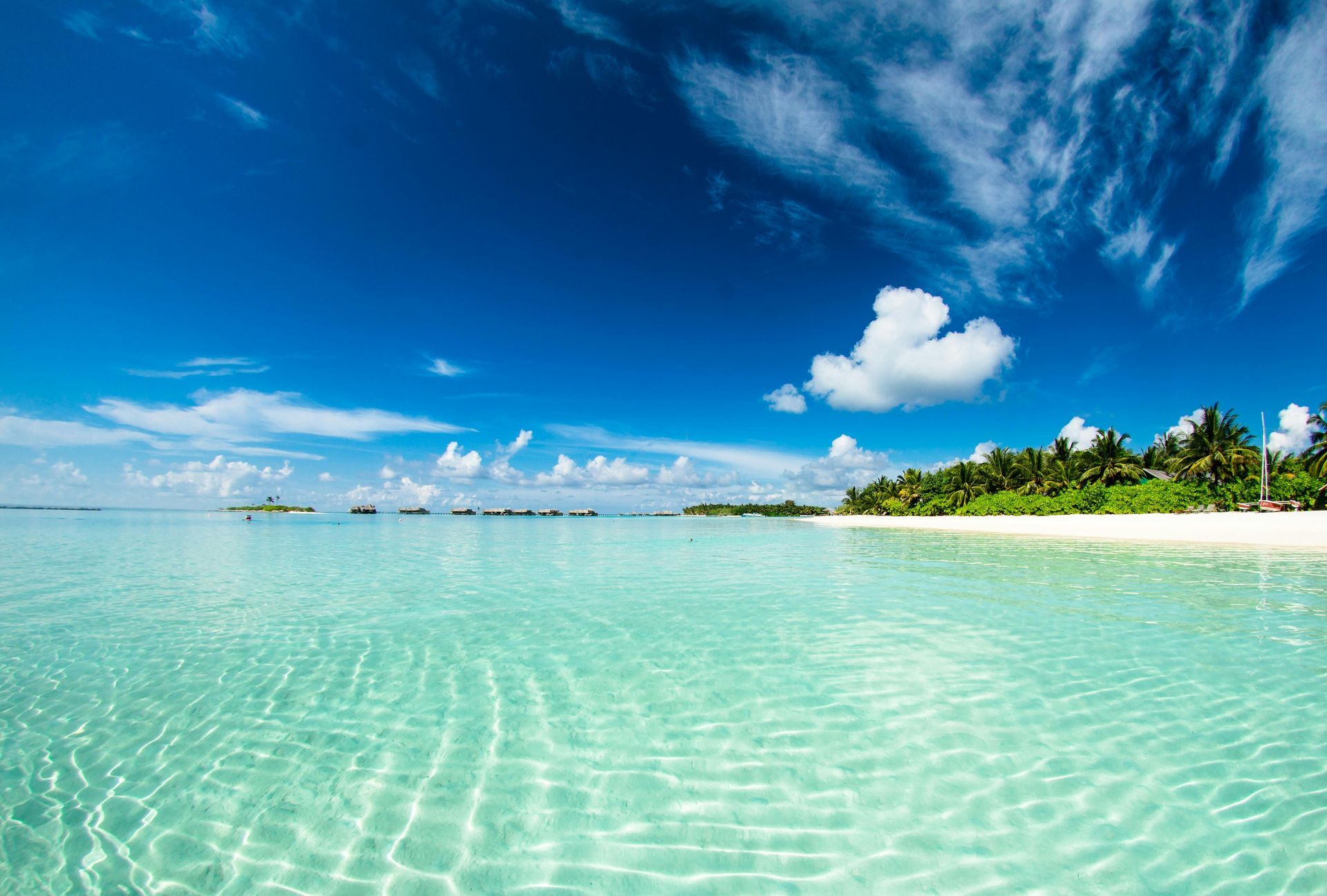 Crystal clear turquoise water and white sand beach under a bright blue sky with clouds.
