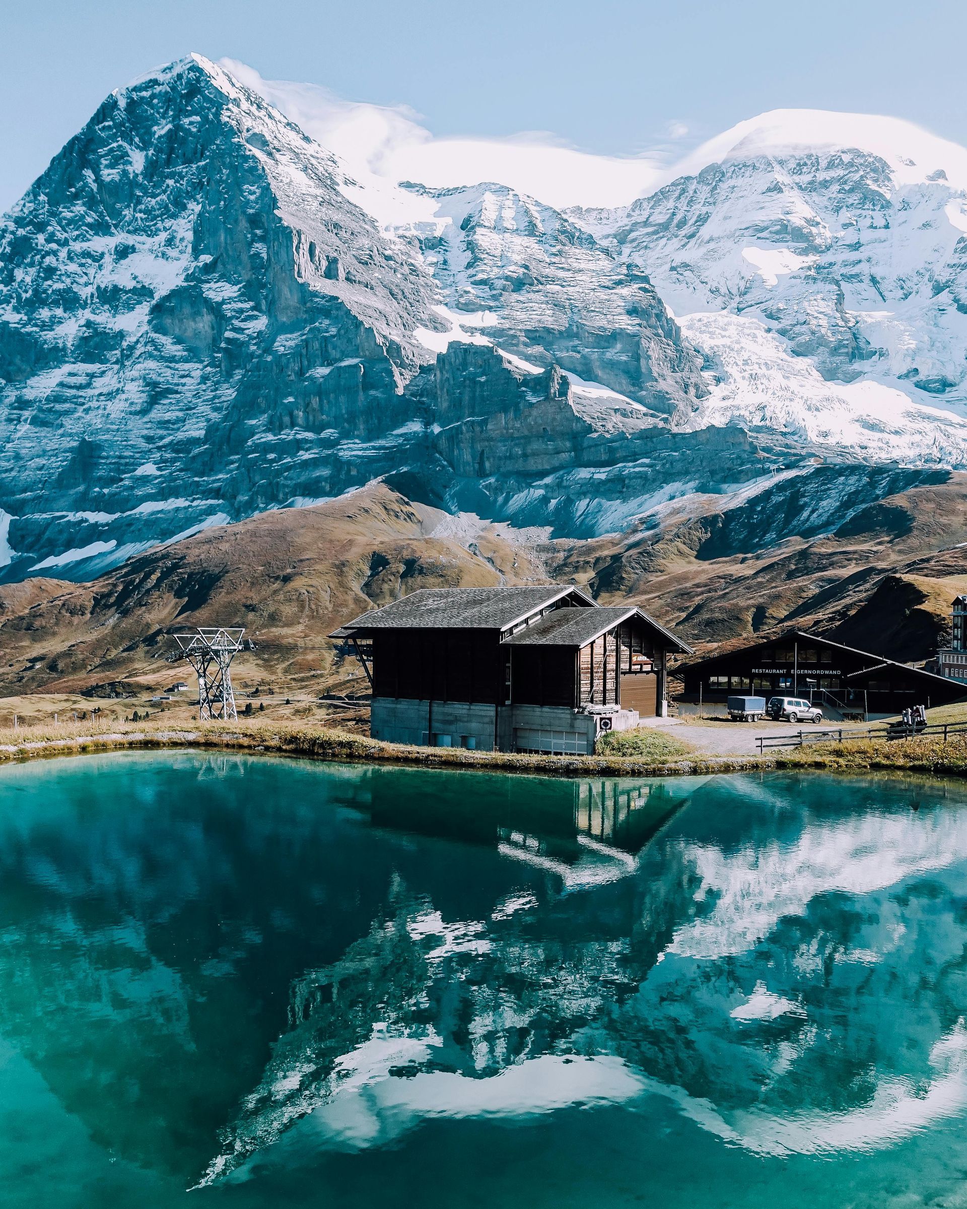 Snowy mountains reflected in turquoise lake with a wooden cabin, in the Alps.
