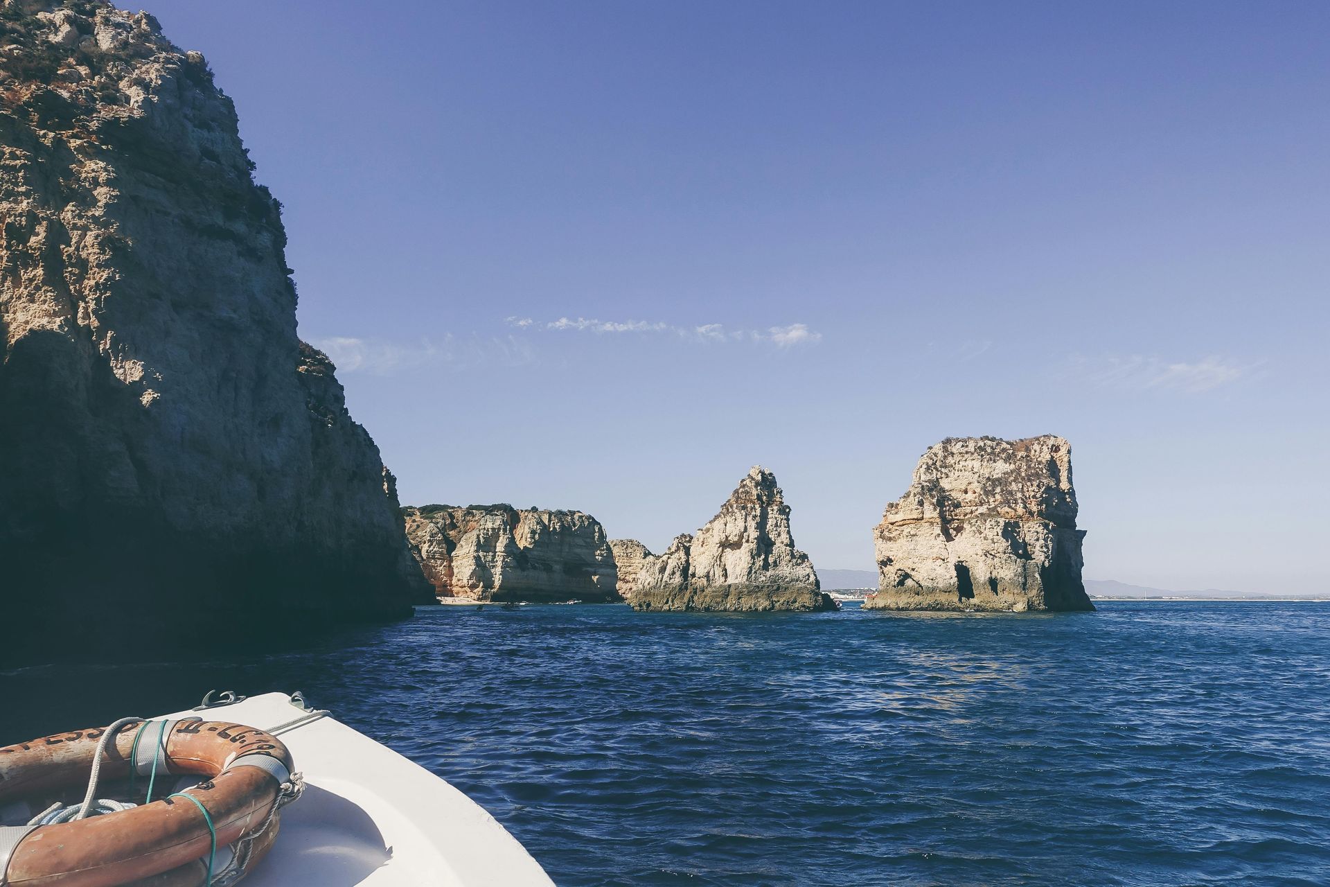 Boat on blue water, passing rock formations on a sunny day.