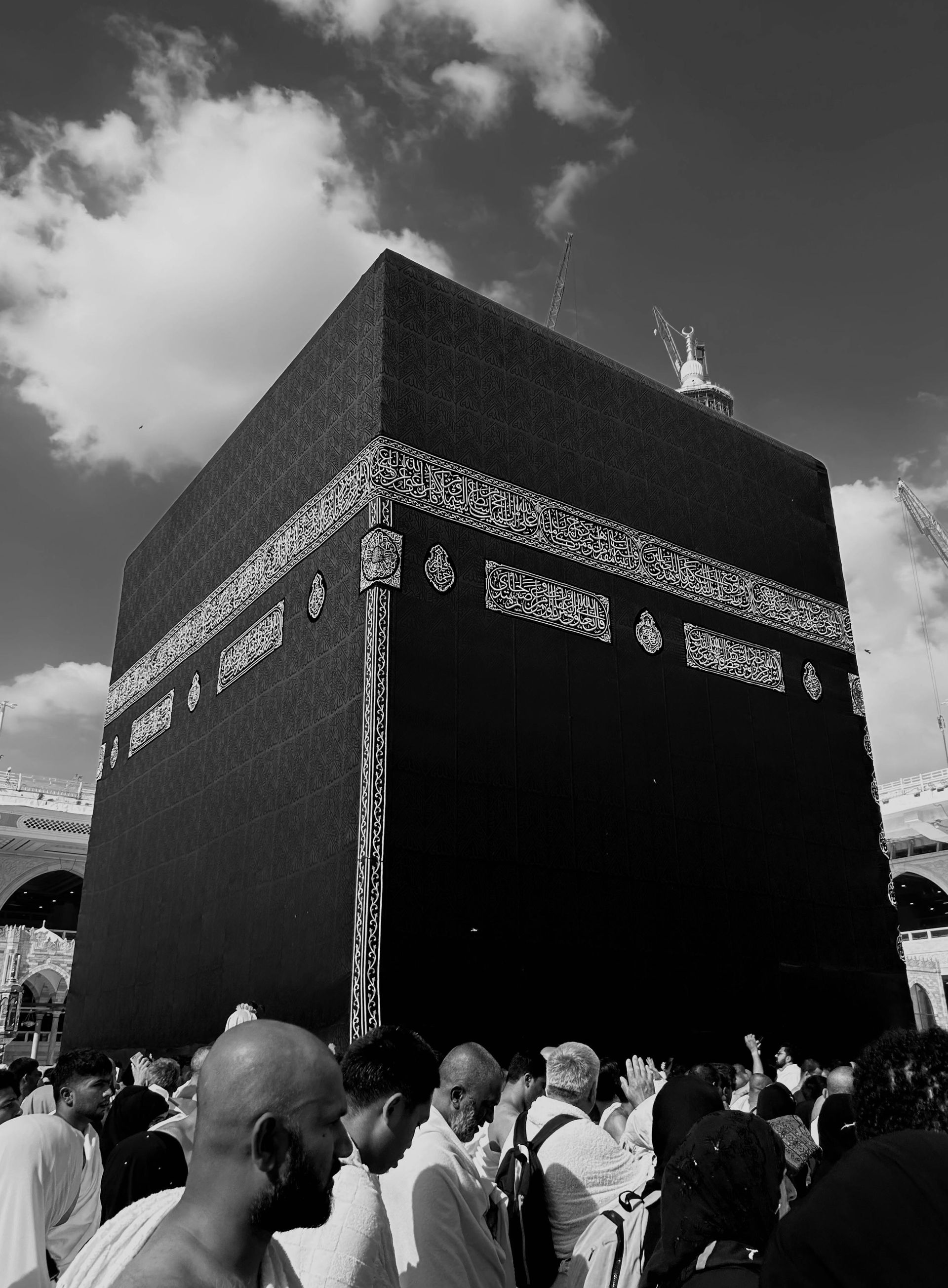 Black and white view of the Kaaba in Mecca, Saudi Arabia, surrounded by people.