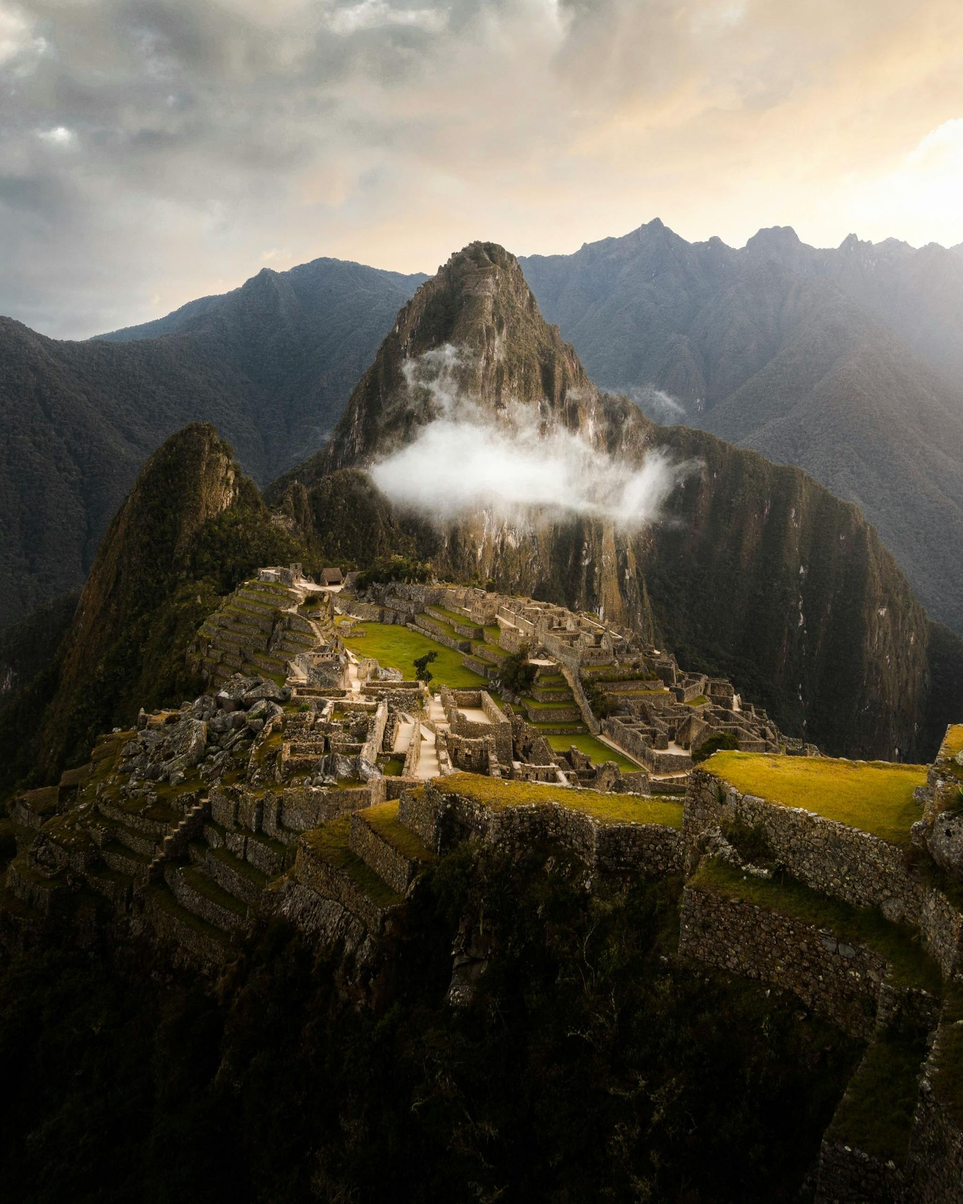 Machu Picchu, ancient Inca city on a mountain peak, Peru. Cloudy sky, stone structures, and green terraces.