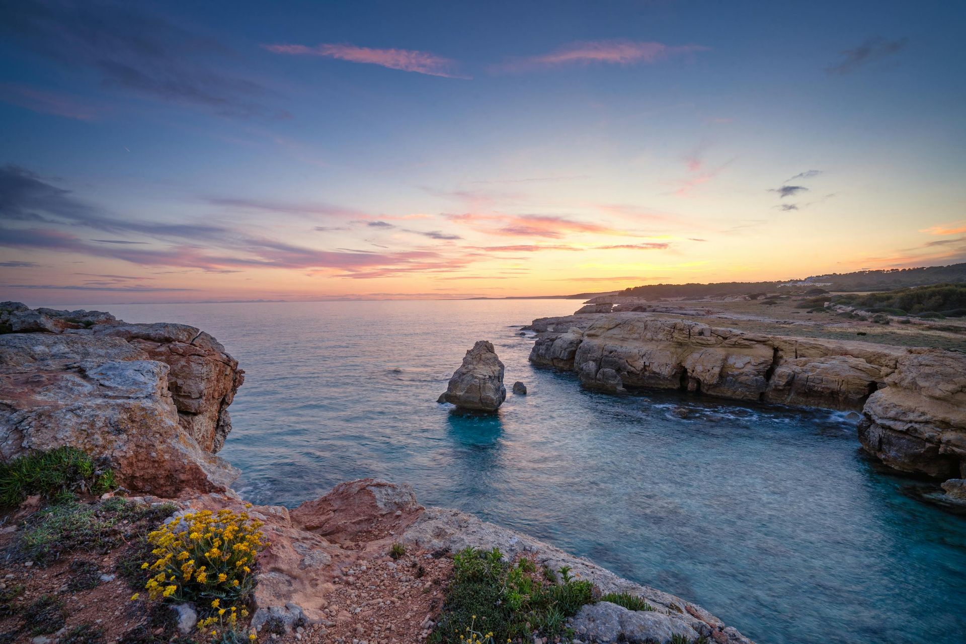 Rocky coastline at sunset with calm blue water and a vibrant sky.