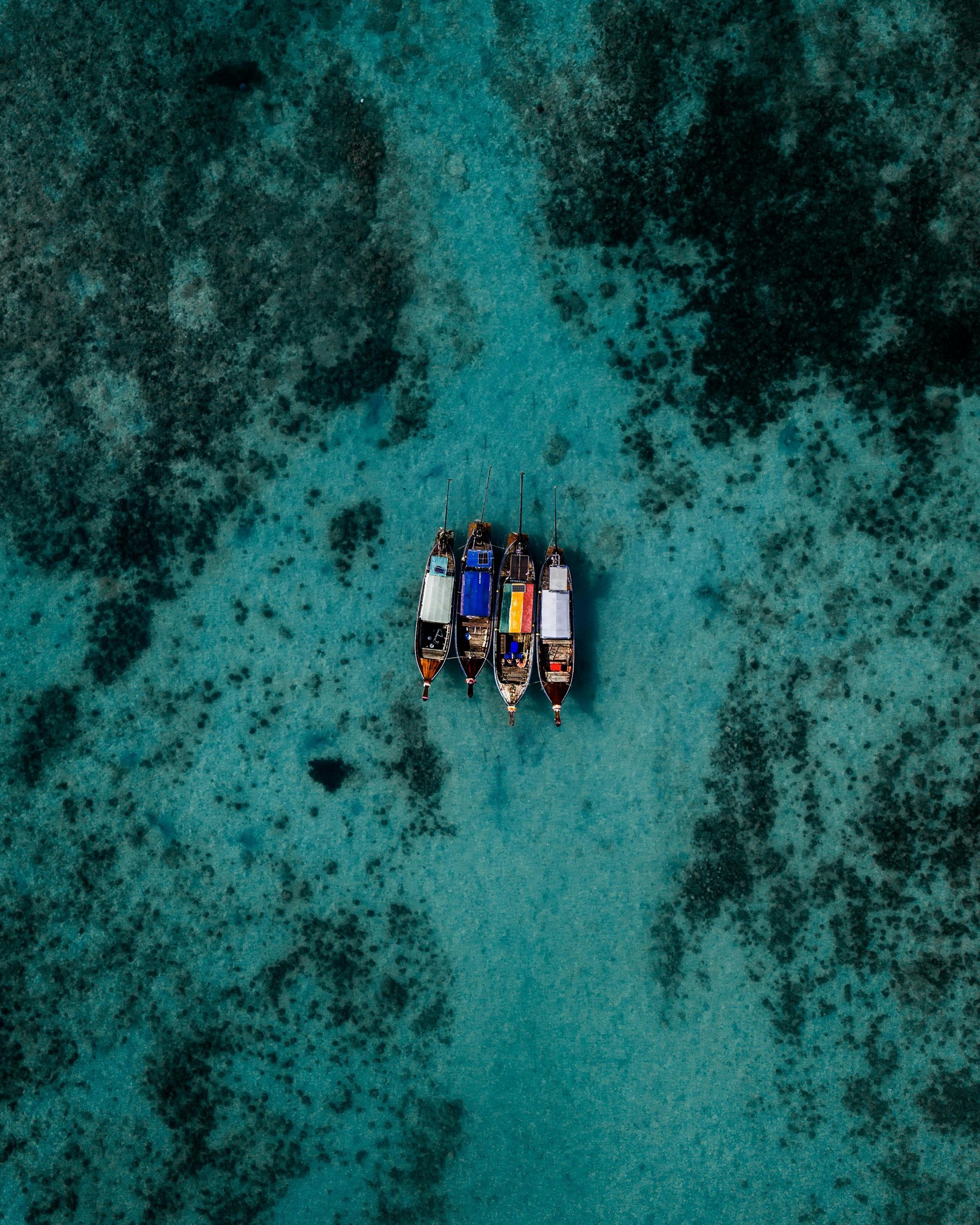 Aerial view of several colorful boats clustered in clear turquoise water over coral reefs.