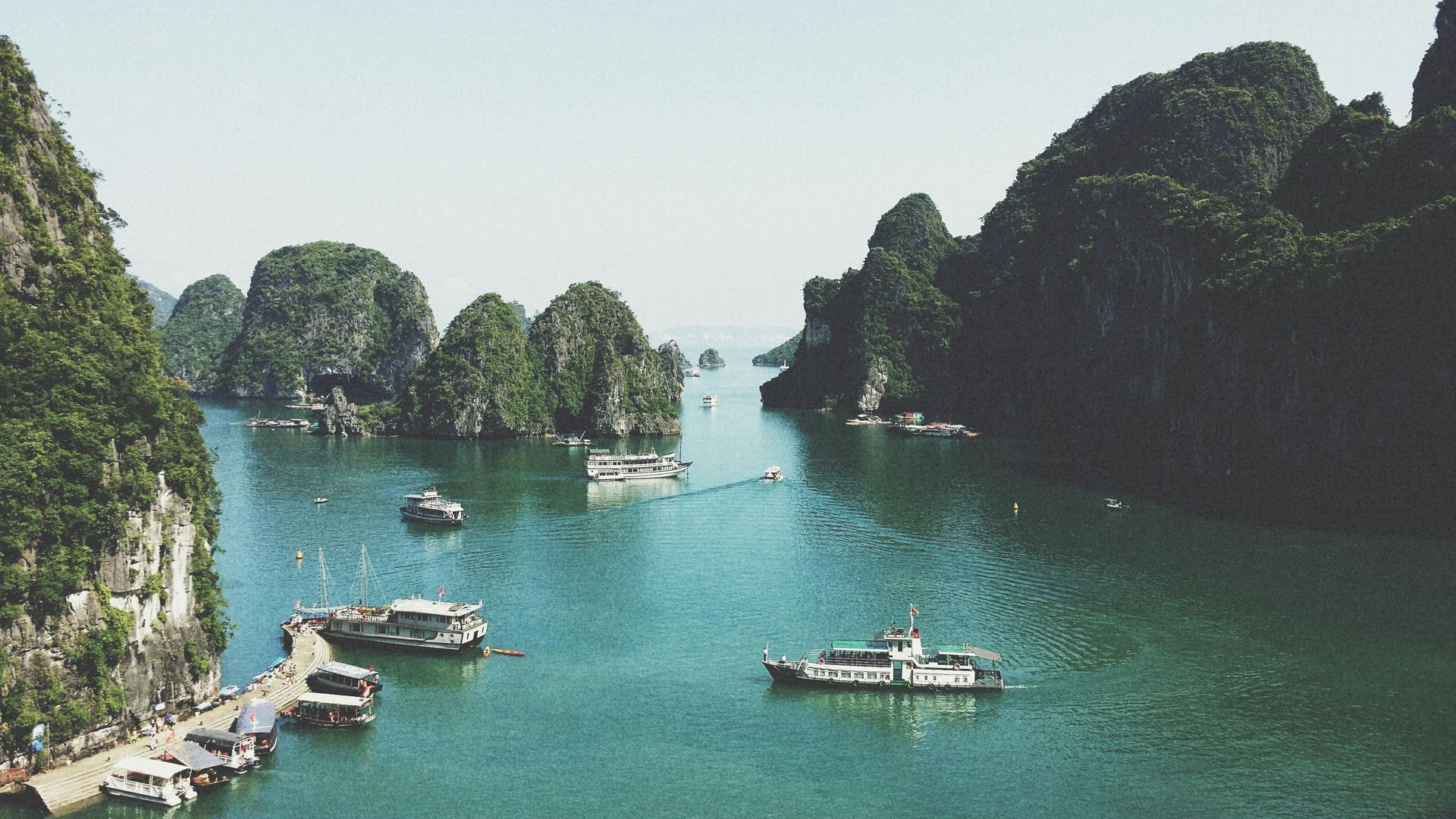 Boats on turquoise water surrounded by limestone karsts in Ha Long Bay, Vietnam.