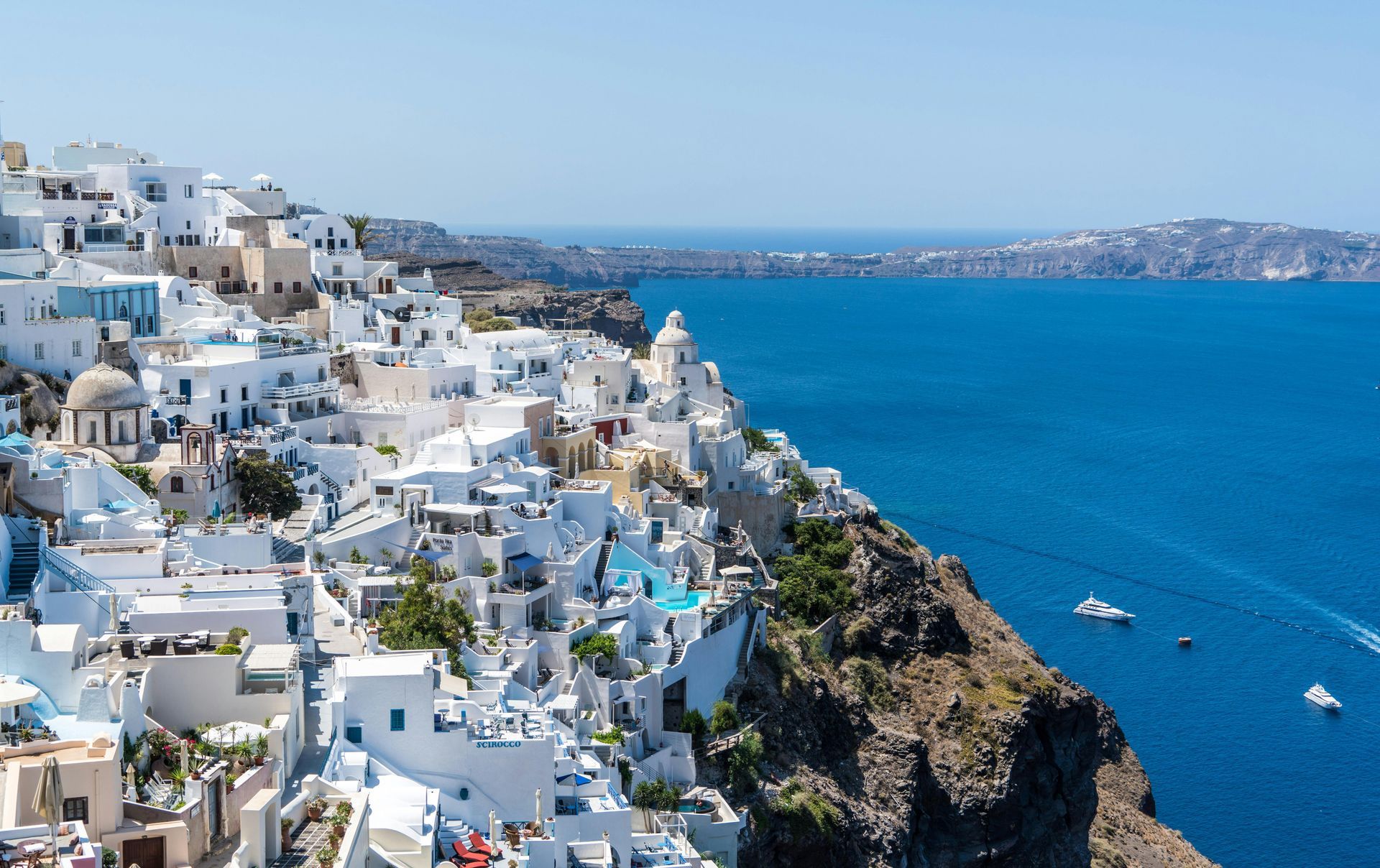 Whitewashed buildings cascade down a cliffside in Santorini, Greece, overlooking the Aegean Sea.