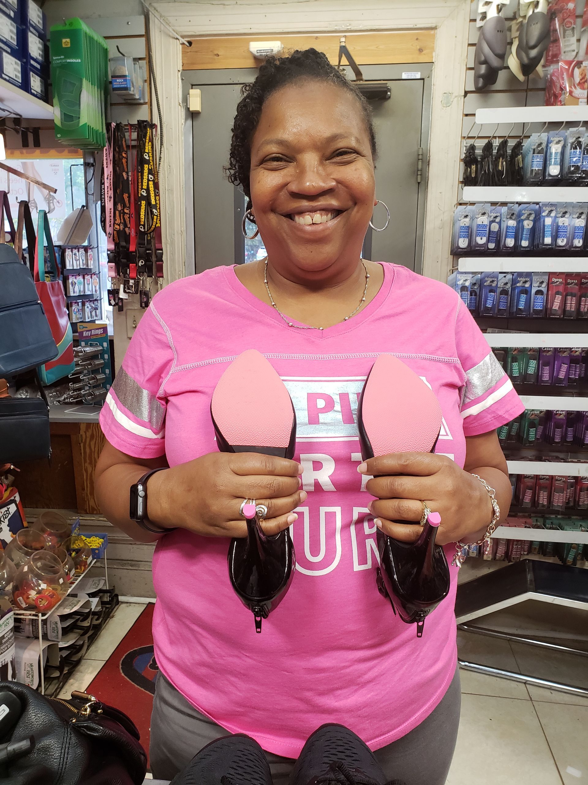 Woman in pink shirt holding two black shoes with pink soles, smiling in a shoe store.