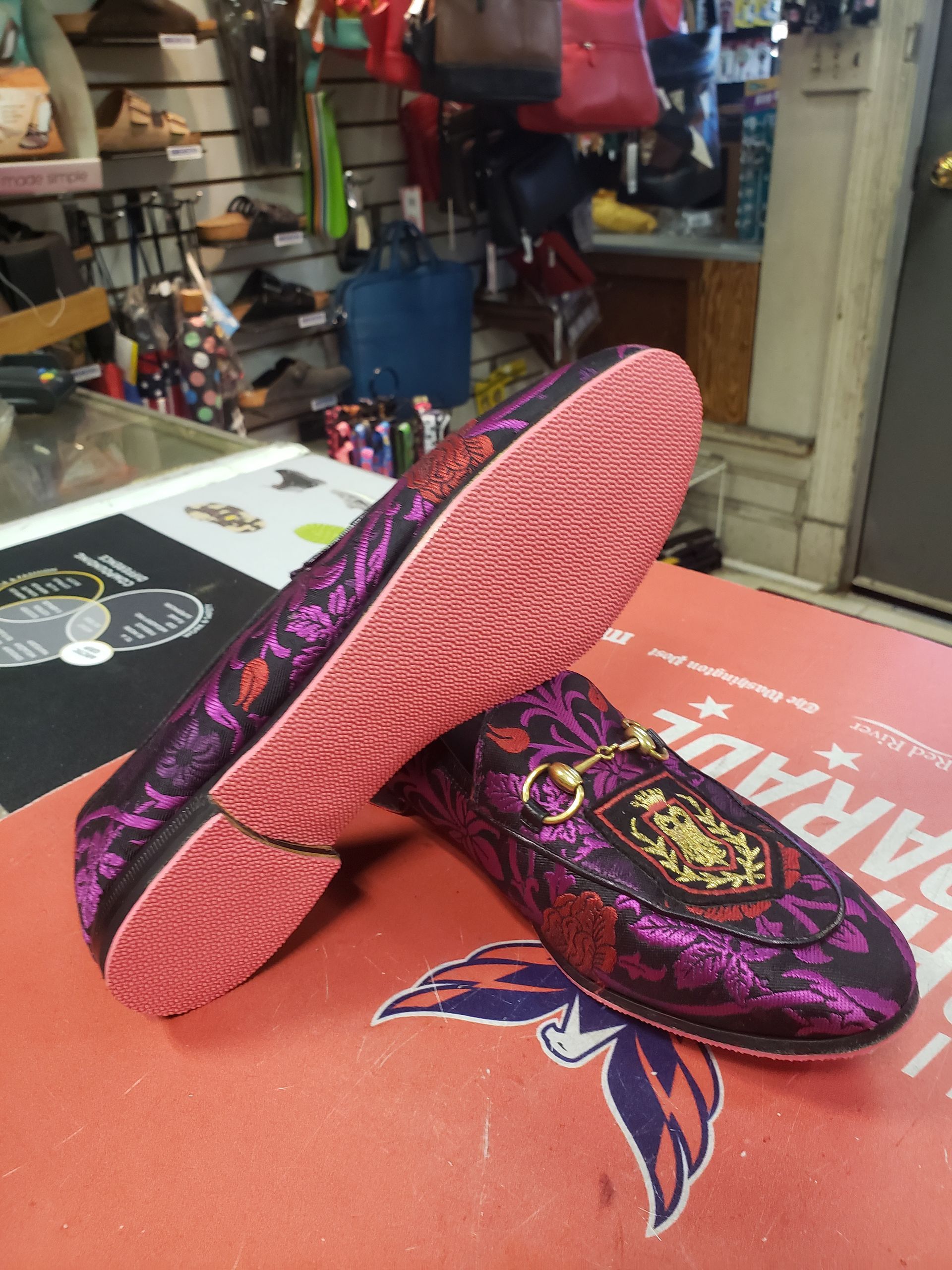 Purple and black patterned loafers with gold accents and a red sole, displayed on a table in a store.
