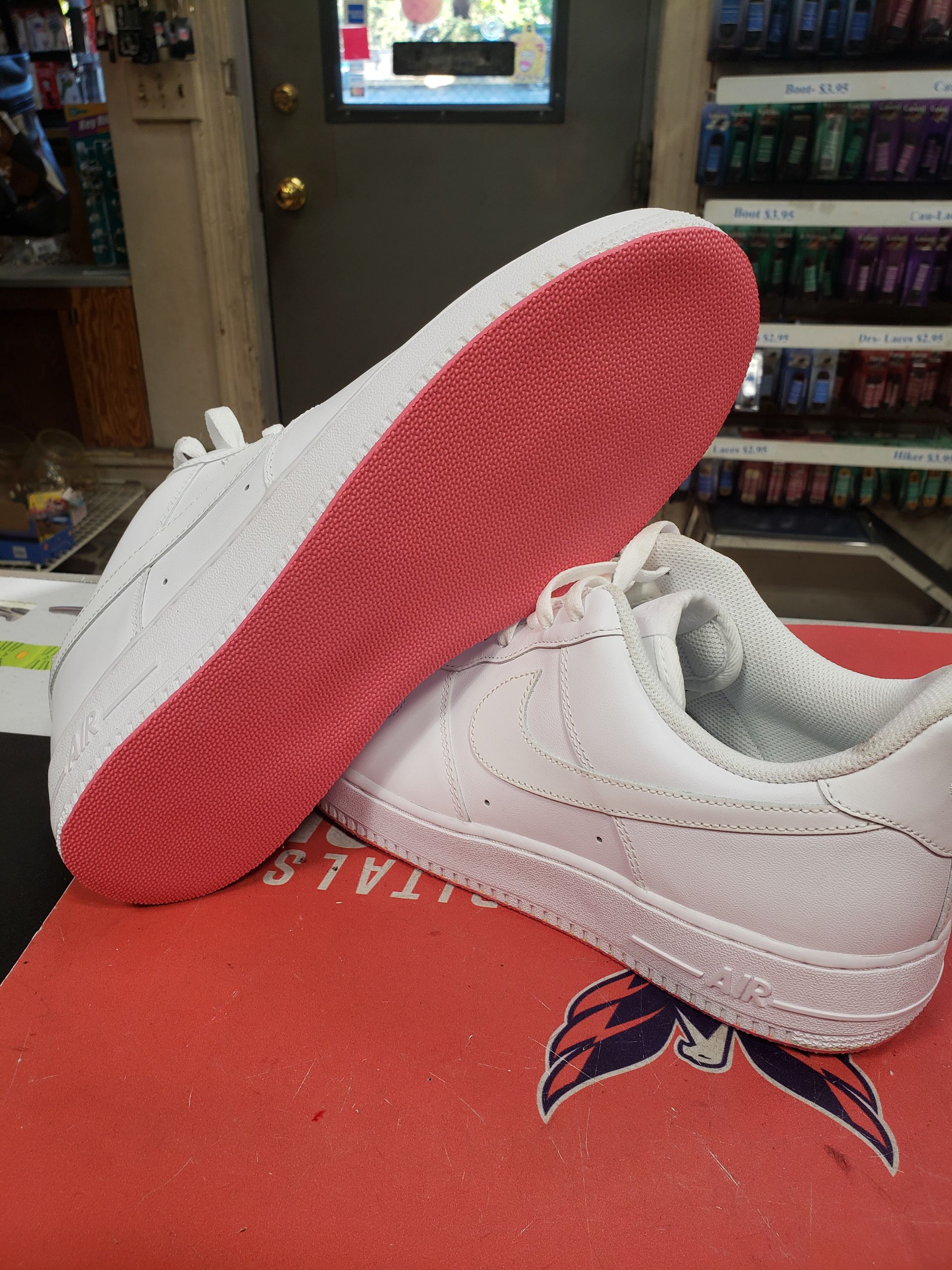 White Nike sneakers with pink soles, resting on a red surface with a logo, indoors.