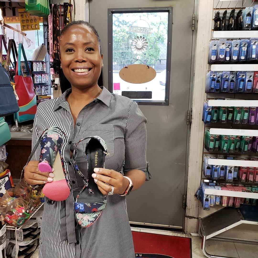 Woman smiling, holding patterned shoes in a shop, wearing a gray and white striped shirt.
