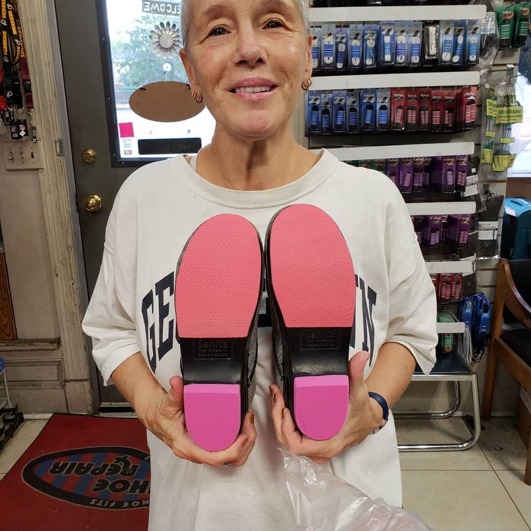 Woman holds up black shoes with pink soles in a store; she smiles.
