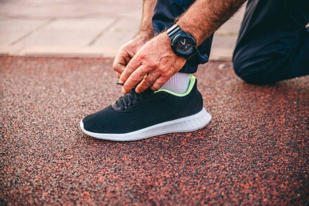 A man tying his shoes on a running track, representing the benefits of customized orthotics in Washi