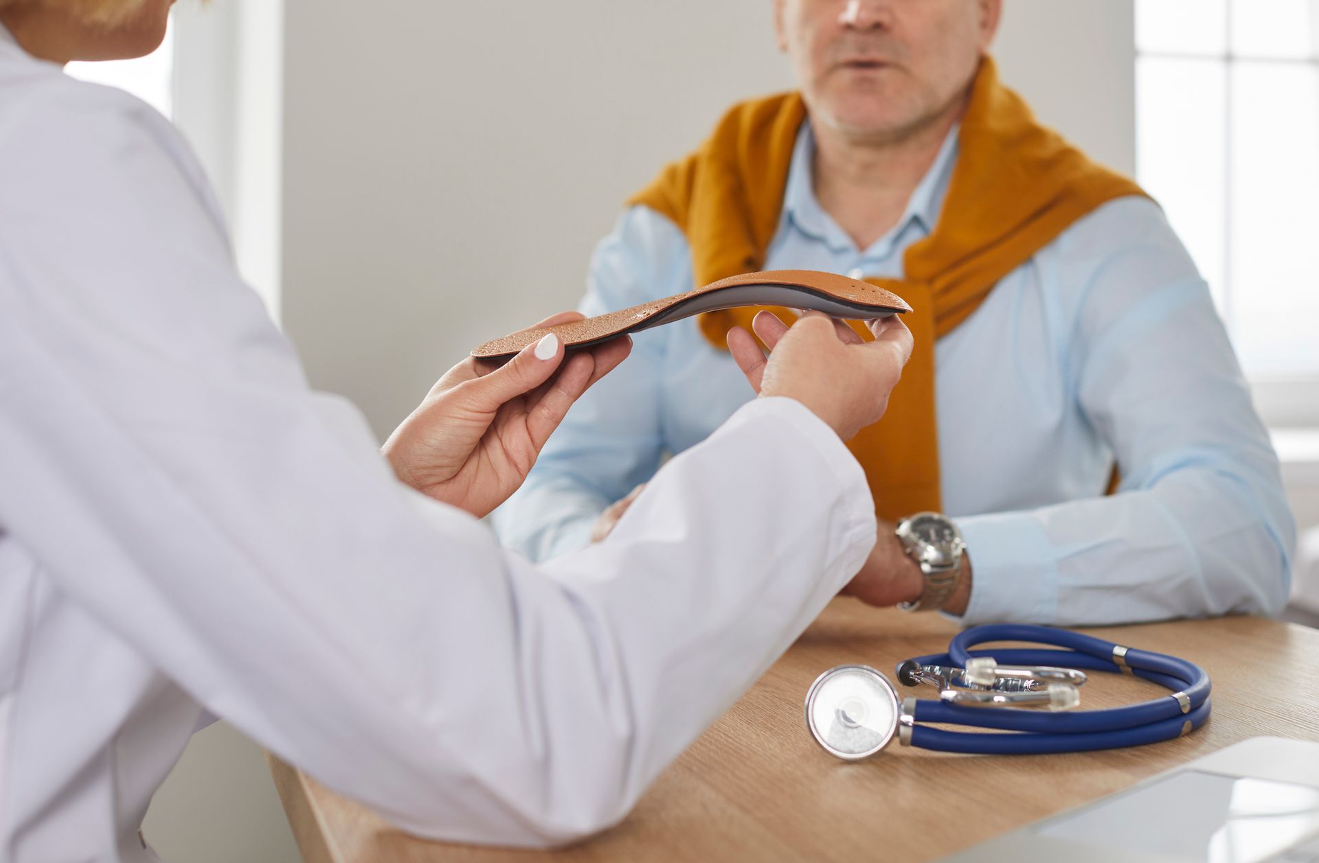 Doctor showing custom orthotics to a senior male patient during a foot health consultation in the clinic.