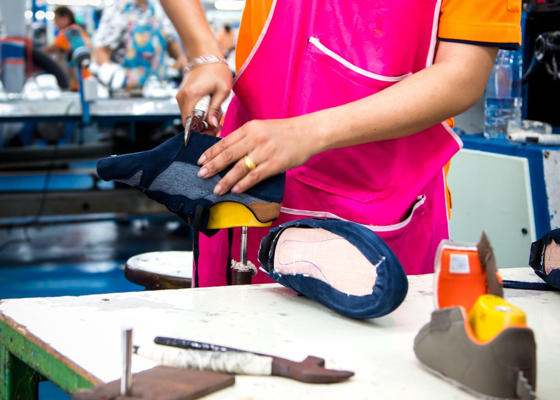 A female worker wearing a pink apron and using a hand tool is working on custom orthotics. A female worker wearing a pink apron and using a hand tool is working on custom orthotics.