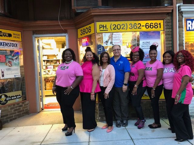 Group of people in pink and black standing outside a shop. Sign and phone number are visible.