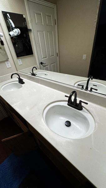Bathroom with double sink vanity, white countertop, black faucets, and large mirror.