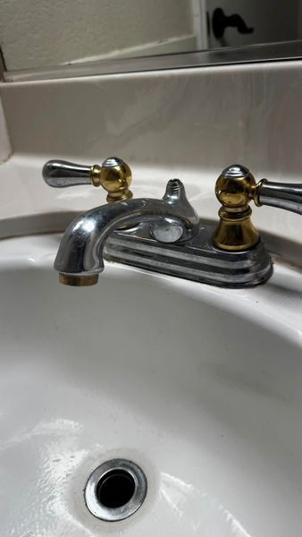 Silver and gold bathroom faucet over a white sink.