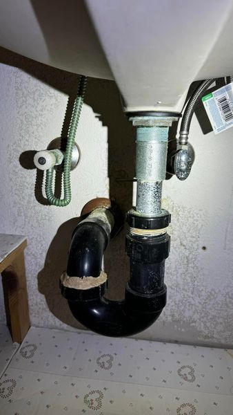 Underside of a sink with plumbing. Black pipes connect to the drain, including a curved P-trap.