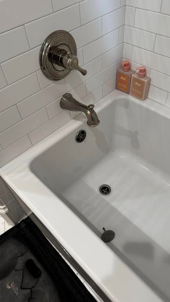White bathtub with silver faucet and handle, against white tile wall; two bottles on the ledge.
