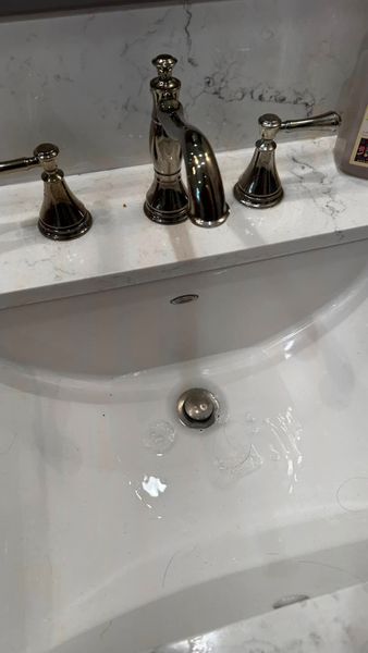 White bathroom sink with a chrome faucet and two handles, water droplets visible.