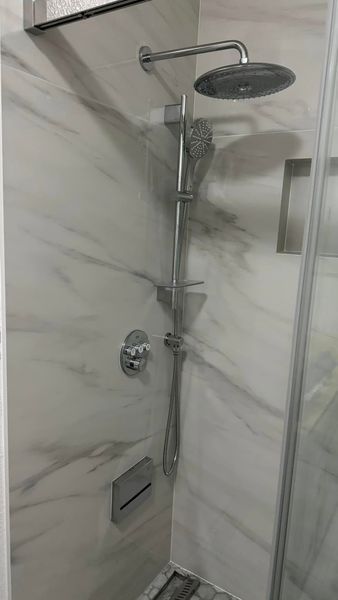 Shower with marble-look tile, overhead rain shower, handheld shower, and soap niche.
