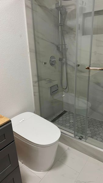 Modern bathroom with a white toilet, shower, and marble tile.