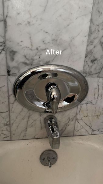 Chrome faucet on a marble tiled wall above a bathtub. 
