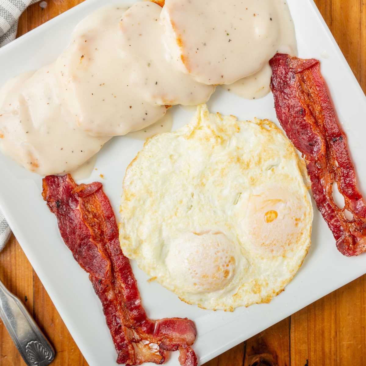a plate of food with eggs , bacon and gravy on a wooden table .