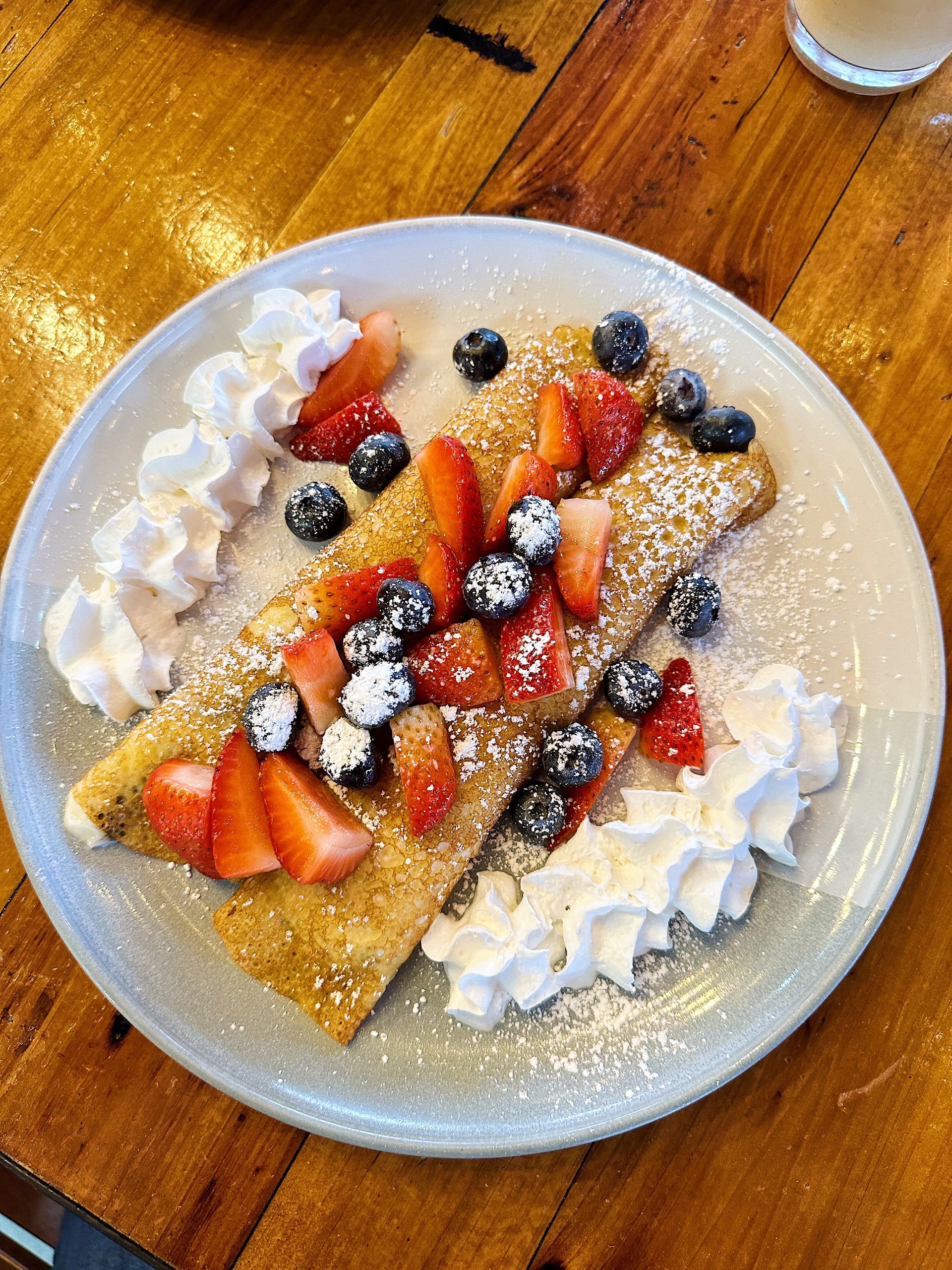 A plate of food with strawberries , blueberries and whipped cream on a wooden table.