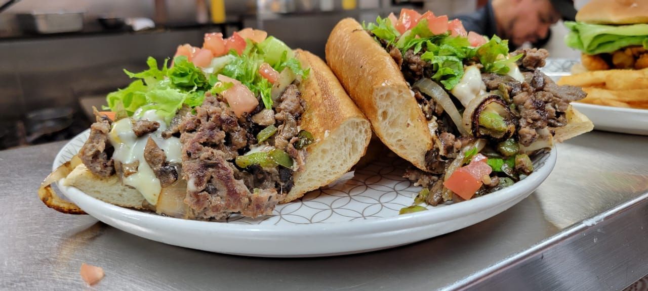 Two steak sandwiches on a plate with lettuce, tomatoes, and herbs, served with fries in the background