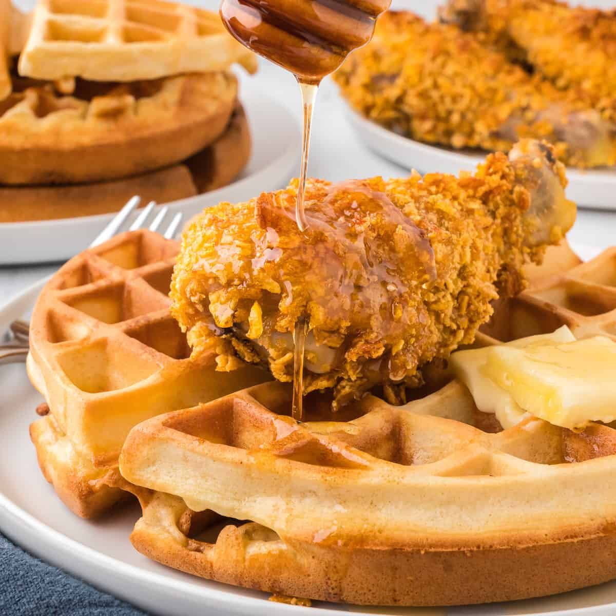 a plate of fried chicken and waffles with syrup being poured on top .