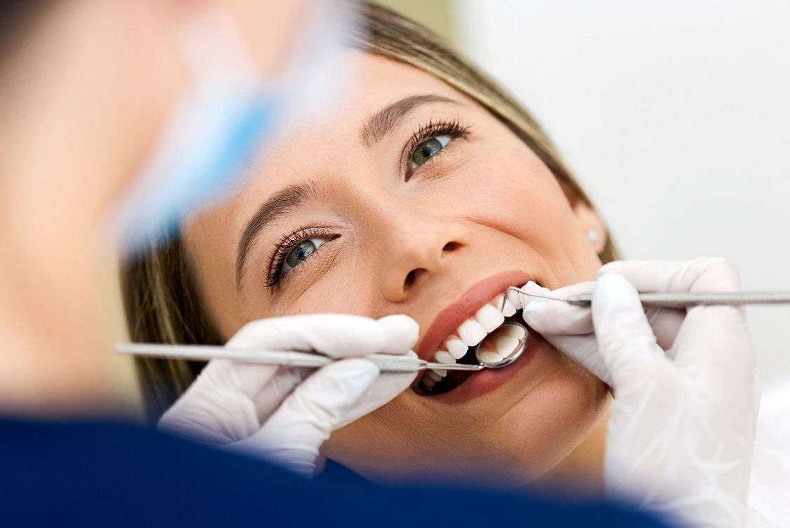 Woman at dentist appointment, smiling while being examined, white gloves and tools.
