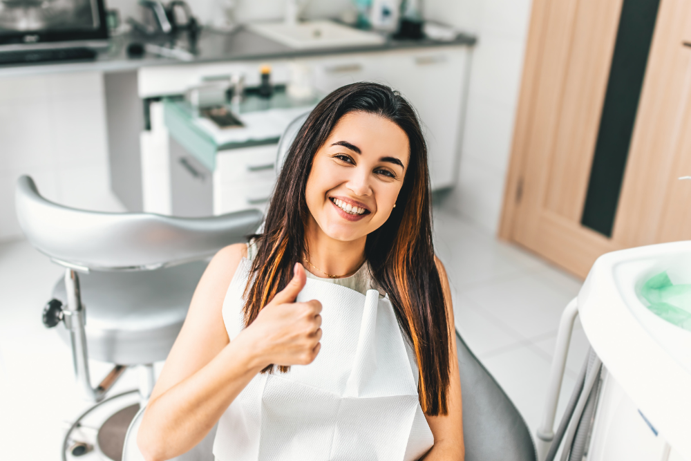 Woman in dentist chair giving thumbs up, smiling.